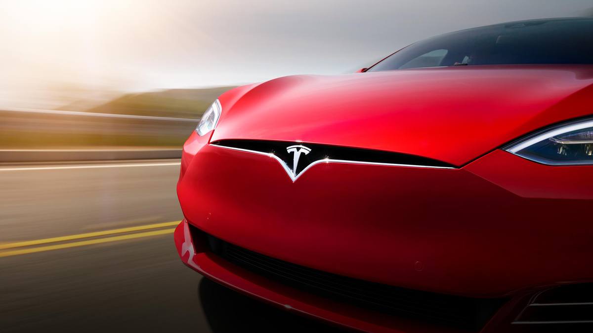 Photograph of a red Tesla model S driving on the road, close up on the front