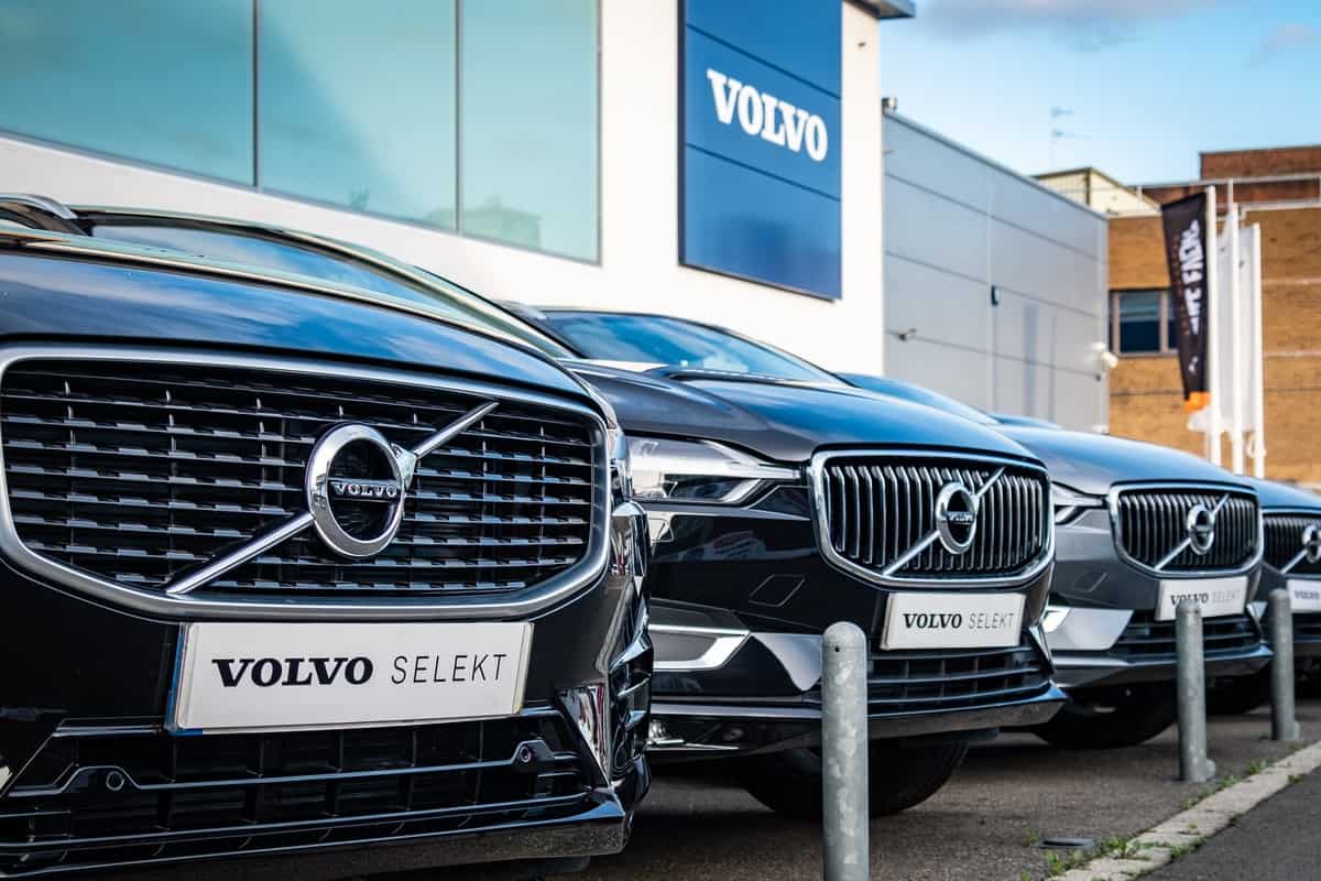 Volvo car dealership, many cars parked outside showroom with Volvo logo above. Swedish vehicle manufacturer