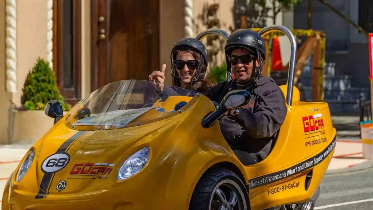 San Francisco, USA - July 18, 2019, joyful tourists close-up in a small yellow car, GoCar is a rental of a 2-seater, 3-wheel car for tourists in San Francisco, California. Tourism, travel concept.