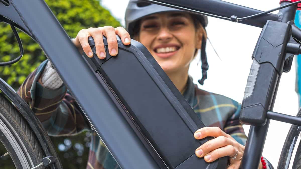 young woman holding an electric bike battery mounted on frame